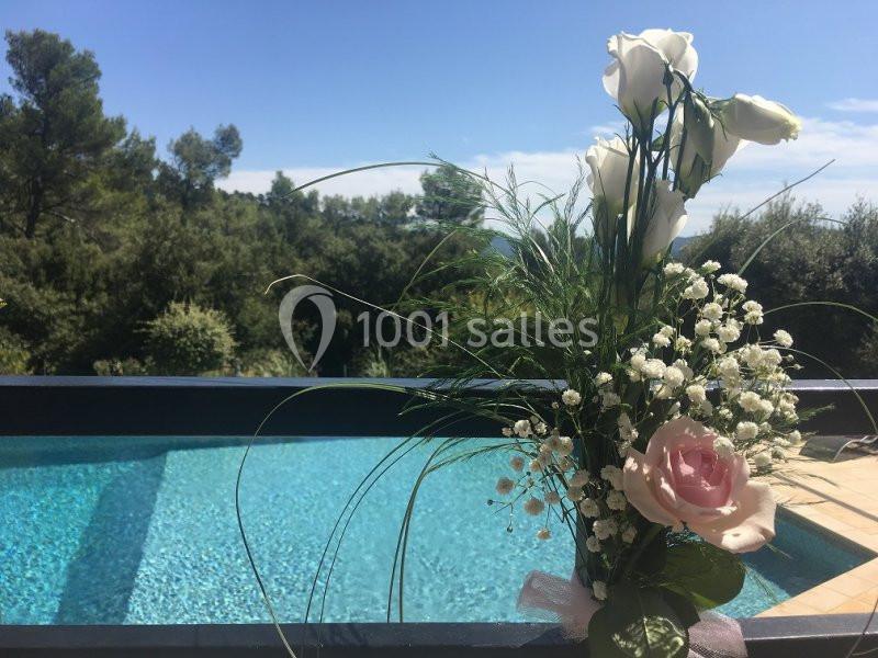 Location salle La Roquebrussanne (Var) - Les Arbousiers #23 Bouquet de fleurs blanches et roses posé près d'une piscine avec vue sur des arbres et un ciel dégagé.