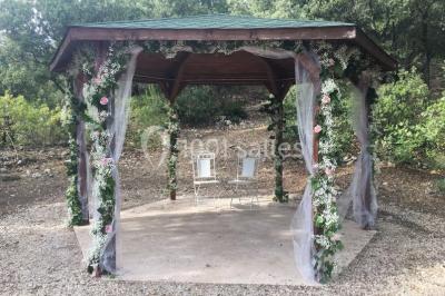 Miniature Location salle La Roquebrussanne (Var) - Les Arbousiers #11 Un couple en tenue de mariage coupe une pièce montée décorée, devant un mur en pierre.