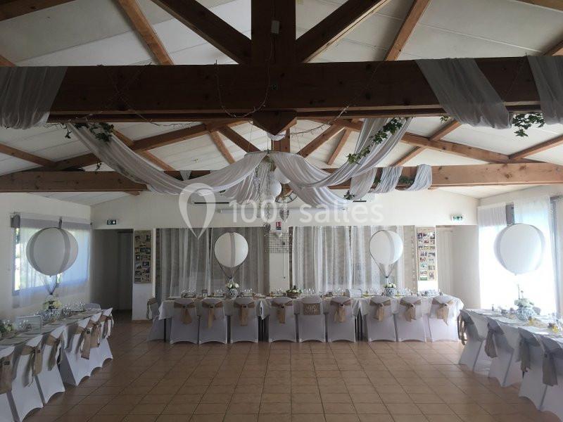Location salle La Roquebrussanne (Var) - Les Arbousiers #28 Salle de réception décorée avec des tables alignées, nappes blanches, chaises ornées et drapés suspendus au plafond.