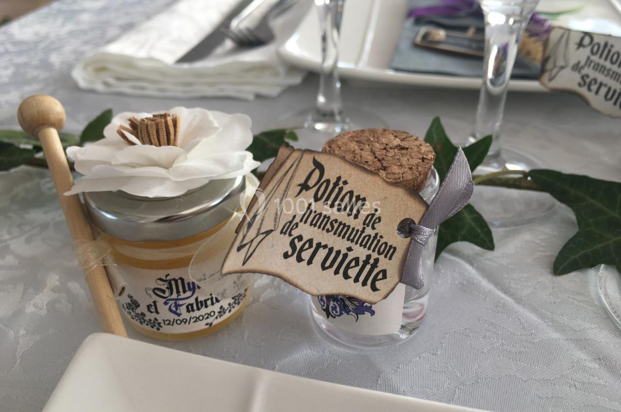 Location salle La Roquebrussanne (Var) - Les Arbousiers #39 Petit pot de miel décoré avec une fleur et une fiole étiquetée ’Potion de transmutation de serviette’ sur une table dressée.