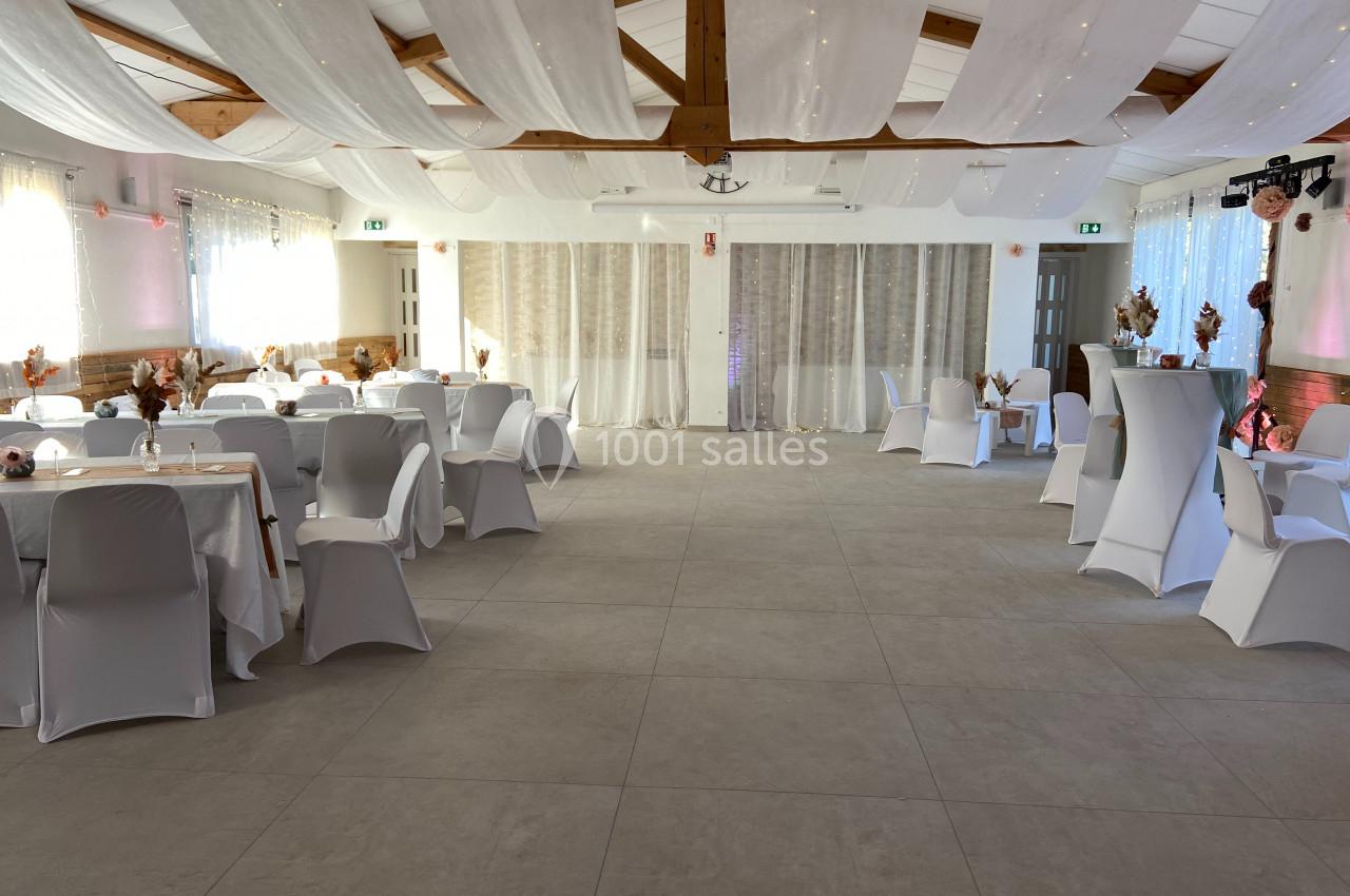 Location salle La Roquebrussanne (Var) - Les Arbousiers #5 Salle de réception décorée avec des tables rondes, nappes blanches, chaises houssées et voilages suspendus au plafond.