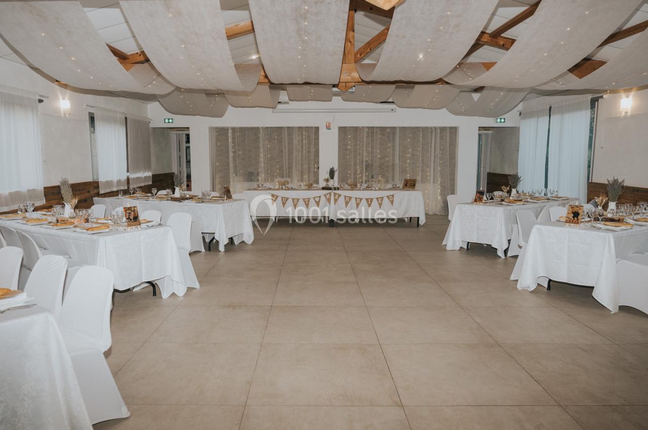 Location salle La Roquebrussanne (Var) - Les Arbousiers #40 Salle de réception décorée avec des tables dressées, nappes blanches et guirlandes suspendues au plafond.