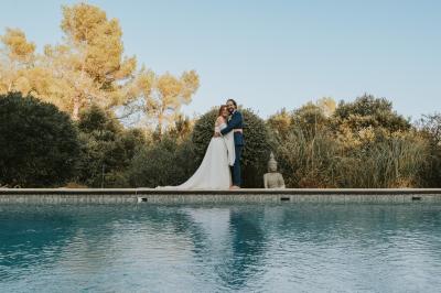 Miniature Location salle La Roquebrussanne (Var) - Les Arbousiers #21 Un couple en tenue de mariage coupe une pièce montée décorée, devant un mur en pierre.