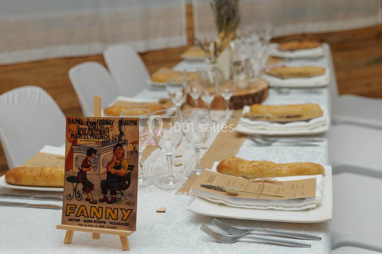 Location salle La Roquebrussanne (Var) - Les Arbousiers #42 Table de réception décorée avec des assiettes, des verres, des baguettes de pain et une affiche rétro sur un chevalet.