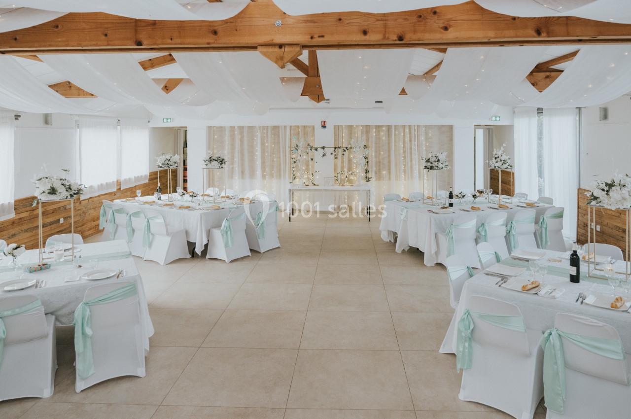 Location salle La Roquebrussanne (Var) - Les Arbousiers #3 Salle de réception décorée avec des tables dressées, des chaises blanches ornées de rubans verts et un plafond drapé.