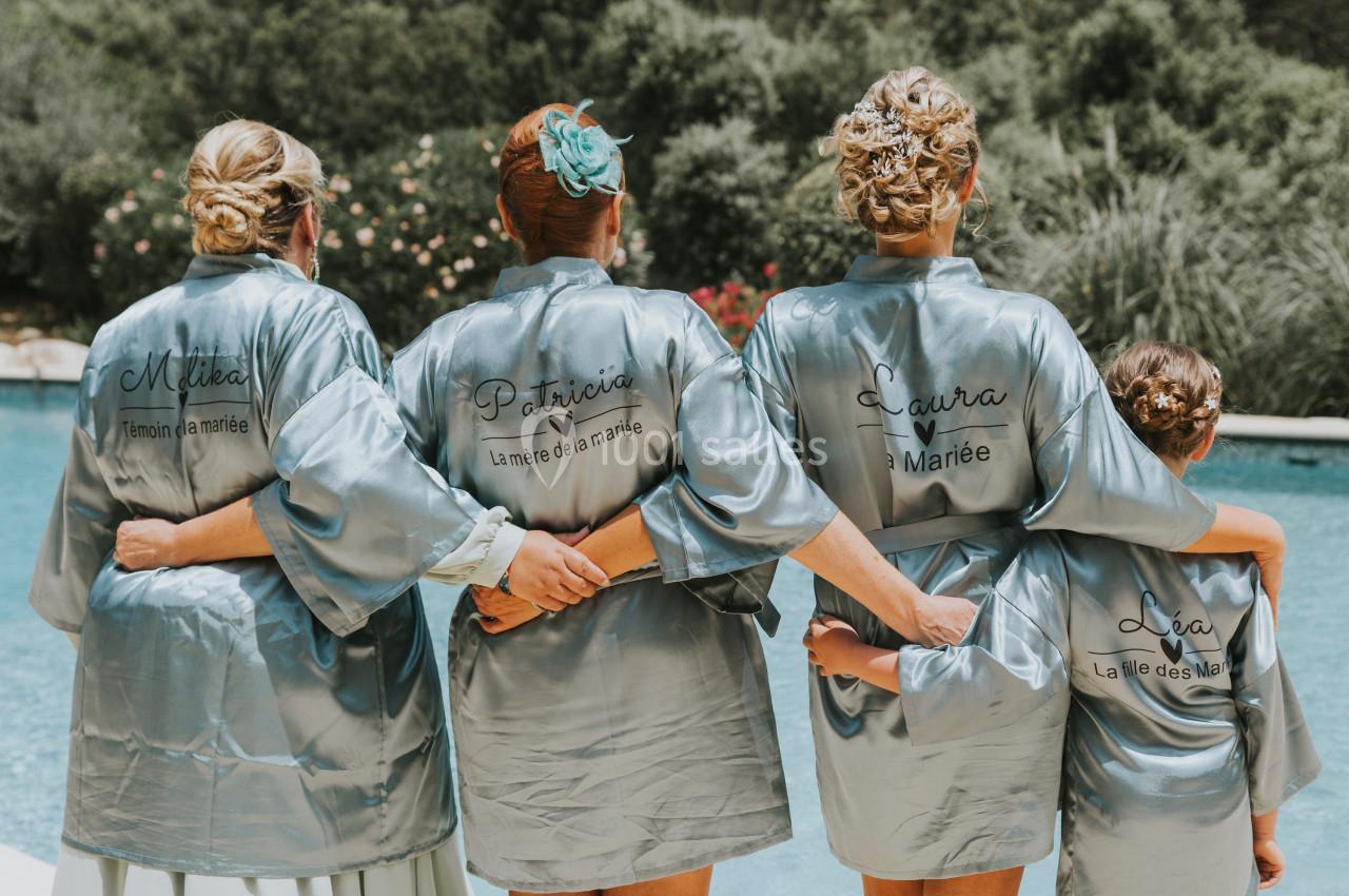 Location salle La Roquebrussanne (Var) - Les Arbousiers #7 Quatre femmes en peignoirs satinés personnalisés, de dos, devant une piscine dans un cadre extérieur verdoyant.