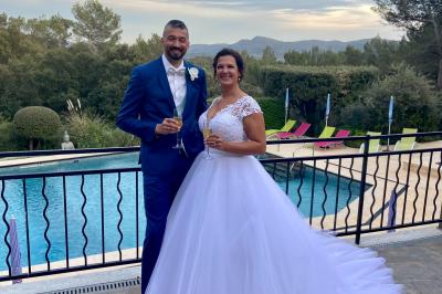 Miniature Location salle La Roquebrussanne (Var) - Les Arbousiers #22 Un couple en tenue de mariage coupe une pièce montée décorée, devant un mur en pierre.