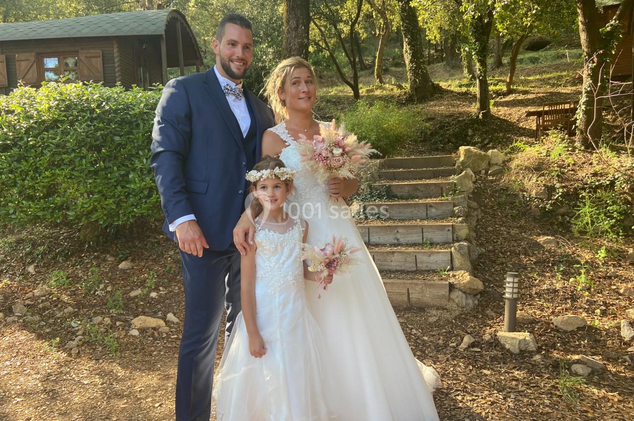 Location salle La Roquebrussanne (Var) - Les Arbousiers #6 Un couple en tenue de mariage pose avec une fillette dans un jardin boisé près d'escaliers en pierre.