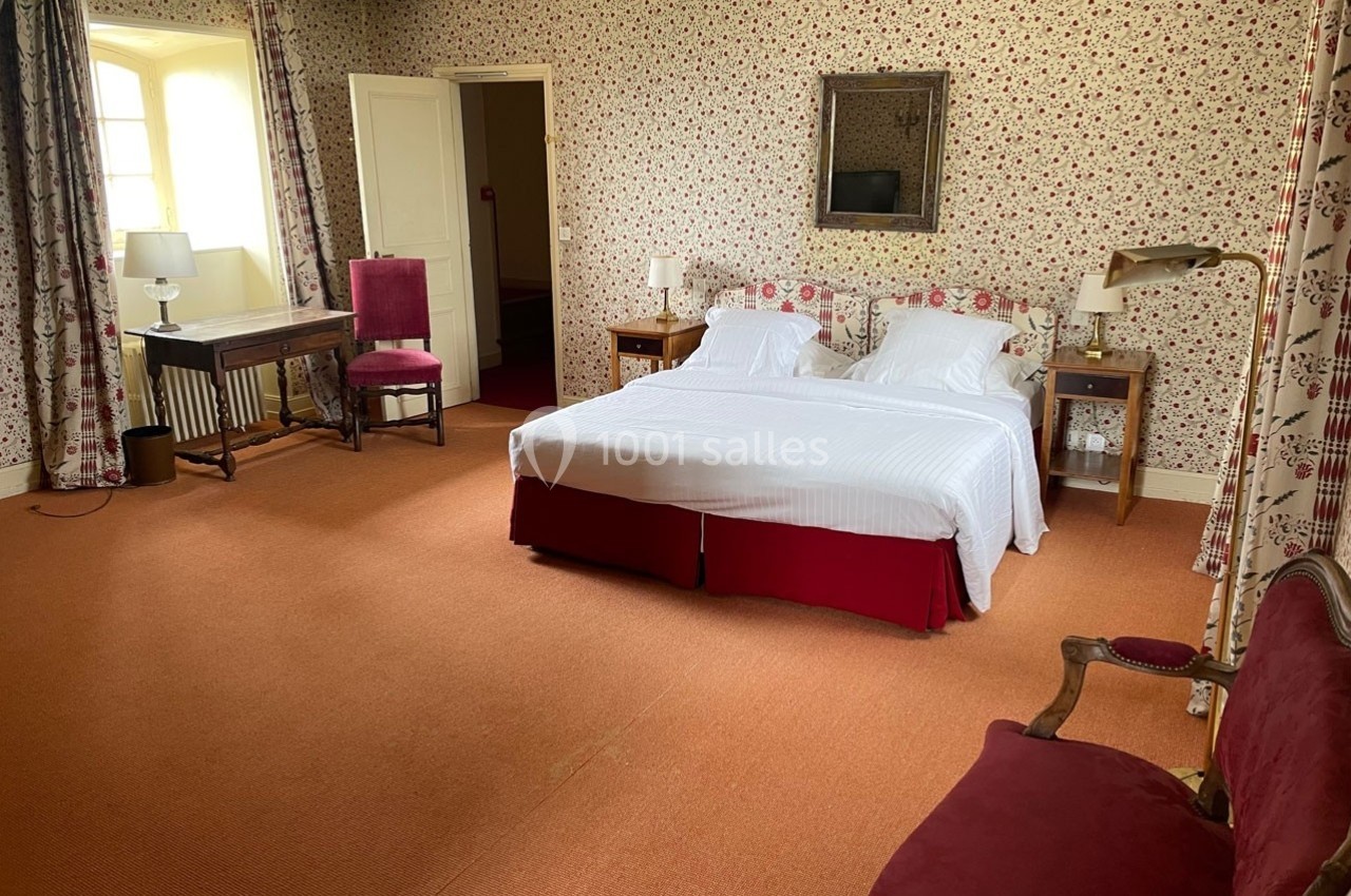 Chambre spacieuse avec lit double, mobilier classique, tapis rouge et murs ornés de papier peint à motifs floraux.