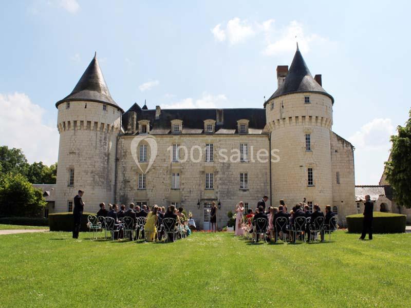 Cérémonie de mariage en plein air devant un château en pierre avec tours rondes, par une journée ensoleillée.