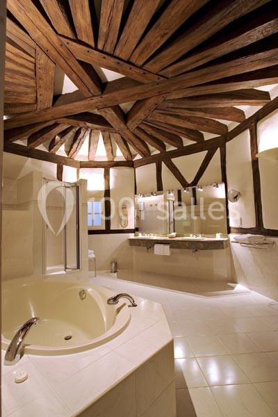 Salle de bain spacieuse avec poutres apparentes, baignoire ronde, douche vitrée et double vasque sur un plan en bois.