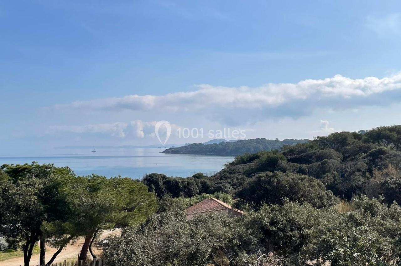 Vue sur une côte boisée avec la mer calme à l'horizon, sous un ciel partiellement nuageux.