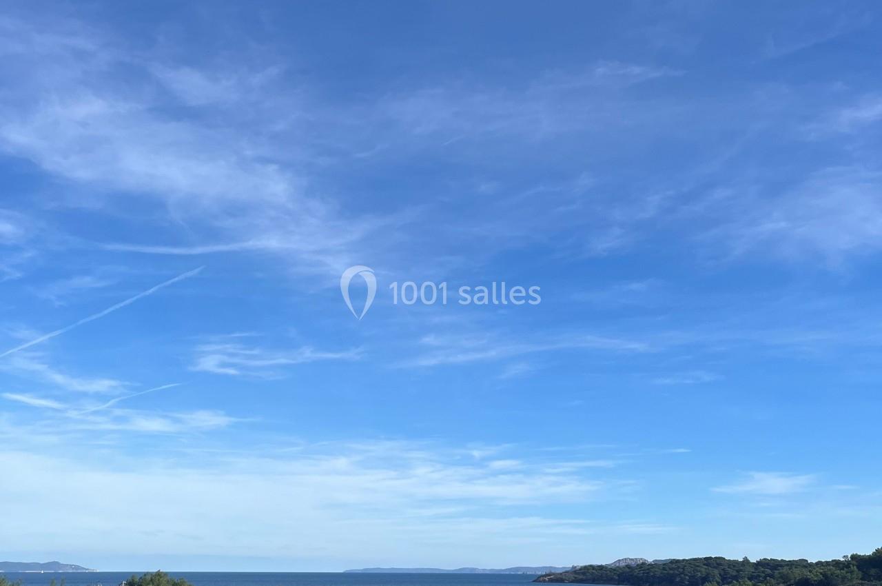 Vue sur une côte méditerranéenne avec des arbres, une plage, la mer et un ciel bleu dégagé.