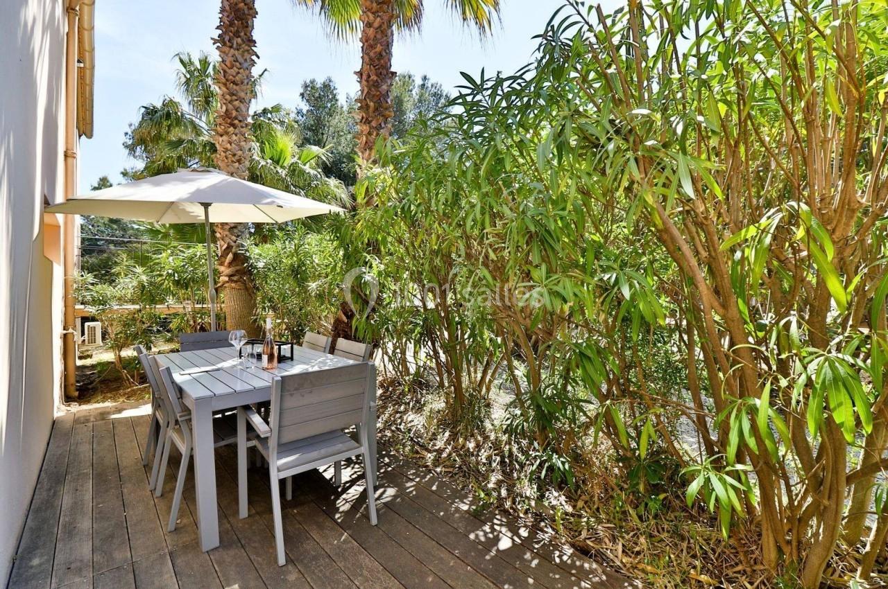 Terrasse en bois avec table, chaises et parasol, entourée de végétation luxuriante et de palmiers.