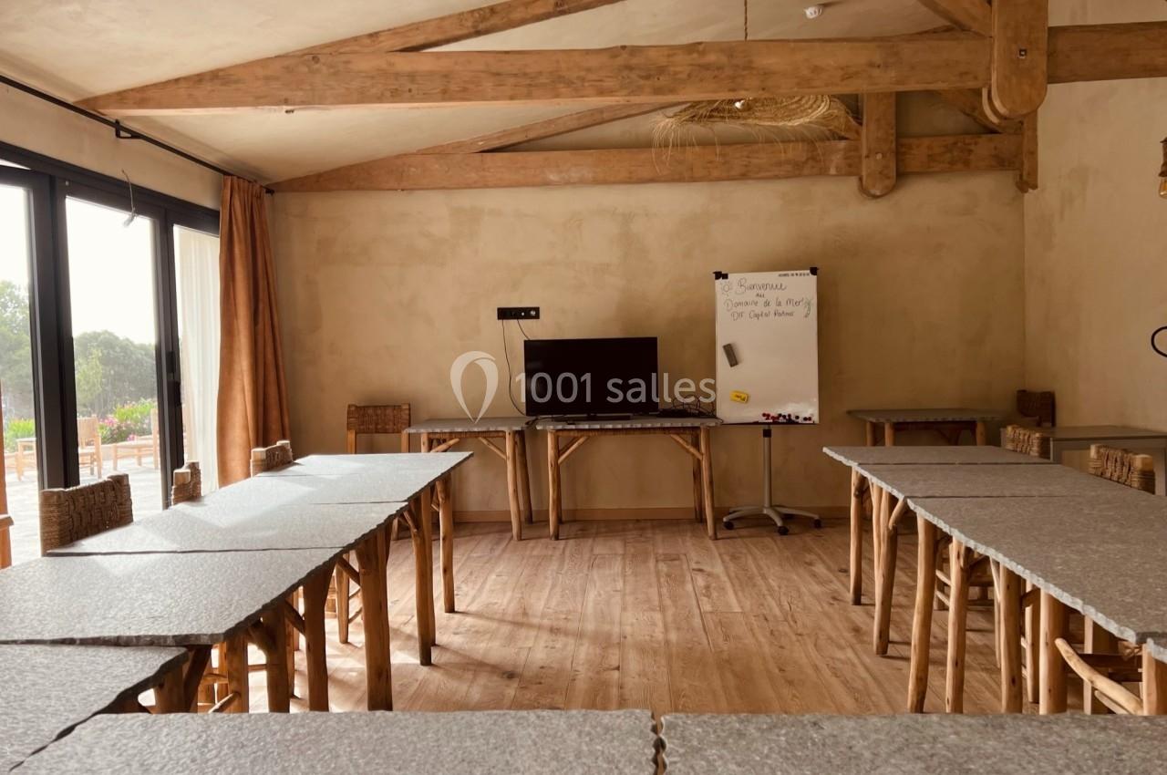Salle de réunion lumineuse avec tables en U, tableau blanc, écran et poutres apparentes en bois.