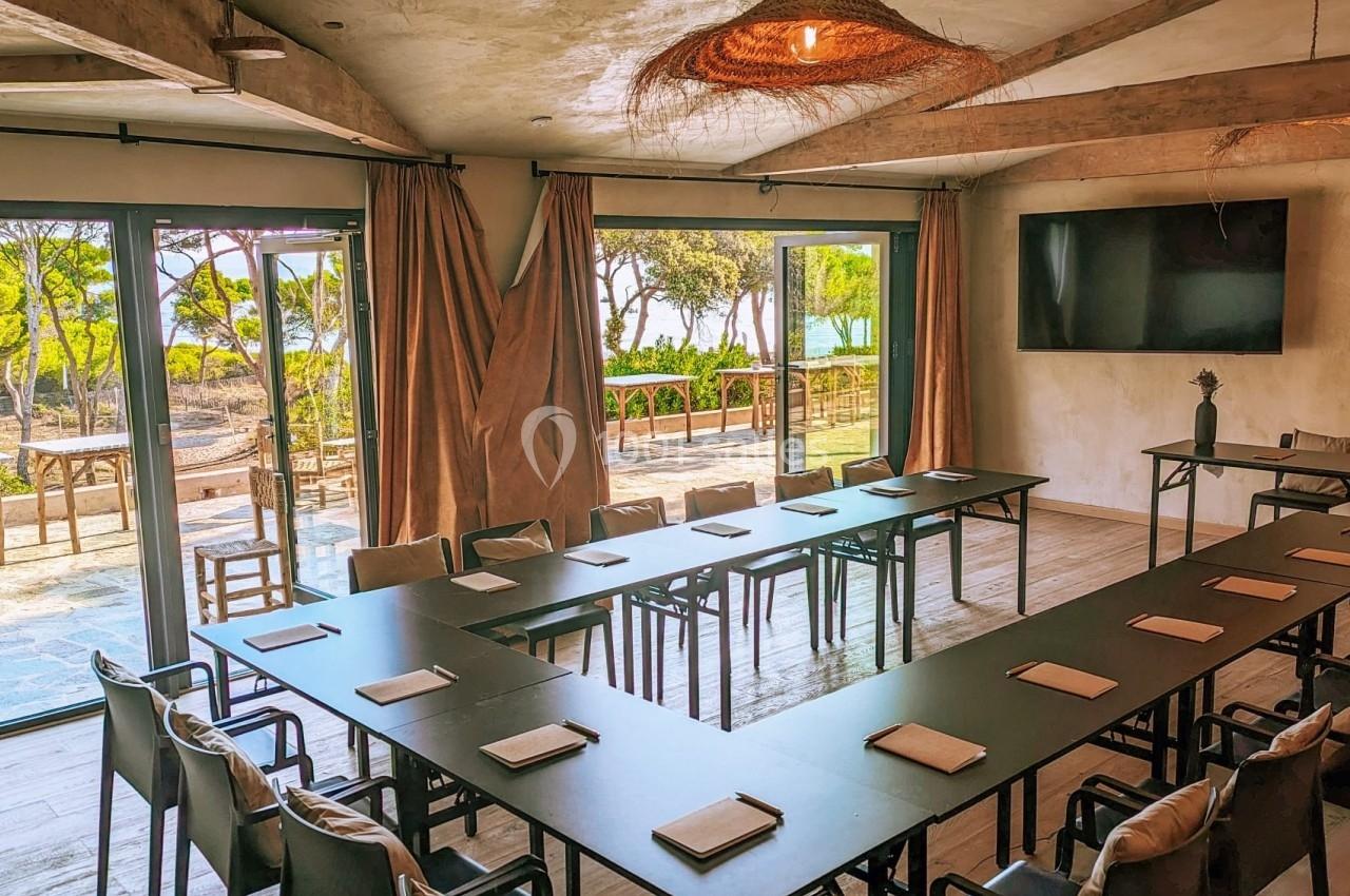 Salle de réunion lumineuse avec grandes baies vitrées, vue sur un espace extérieur arboré et tables disposées en U.