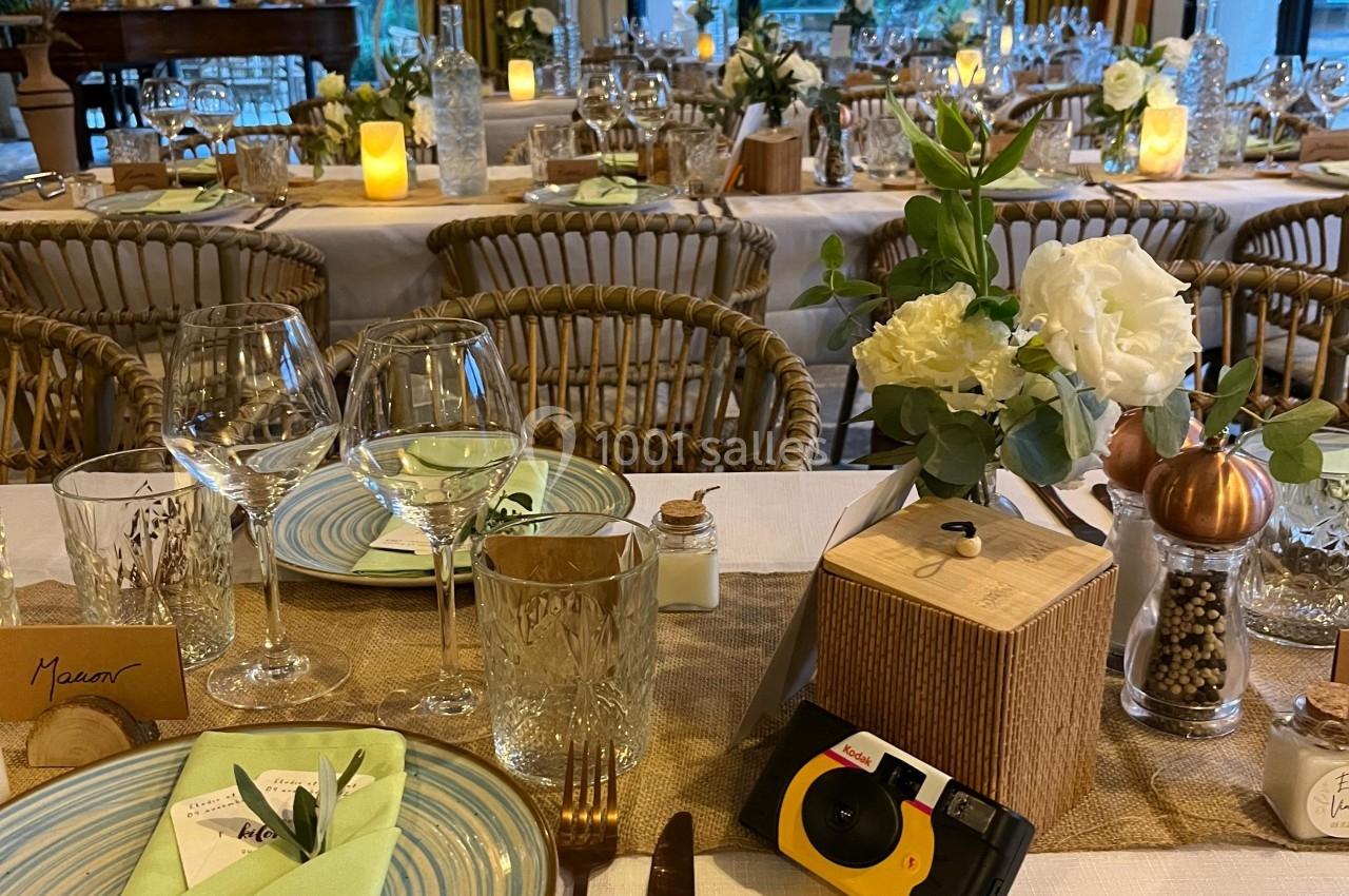 Table dressée pour un repas, avec assiettes, verres, serviettes vertes, décorations florales et appareil photo jetable.