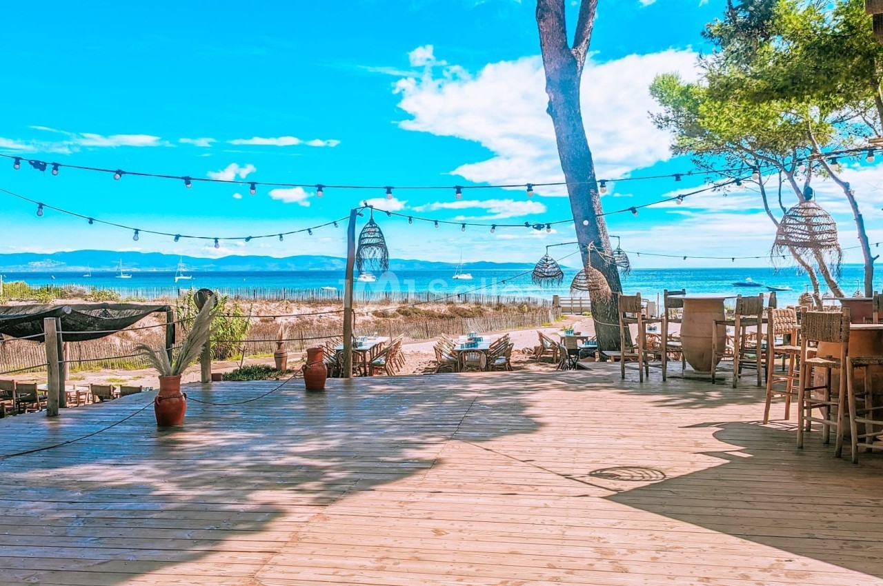 Terrasse en bois avec vue sur la mer, décorée de guirlandes lumineuses et de lampes suspendues, entourée de végétation.