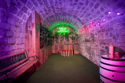 Miniature Location salle Paris 4 (Paris) - Paris Clandestin #10 Fléchettes colorées dans une caisse en bois au premier plan, cible de jeu accrochée sur un mur en pierre en arrière-plan.