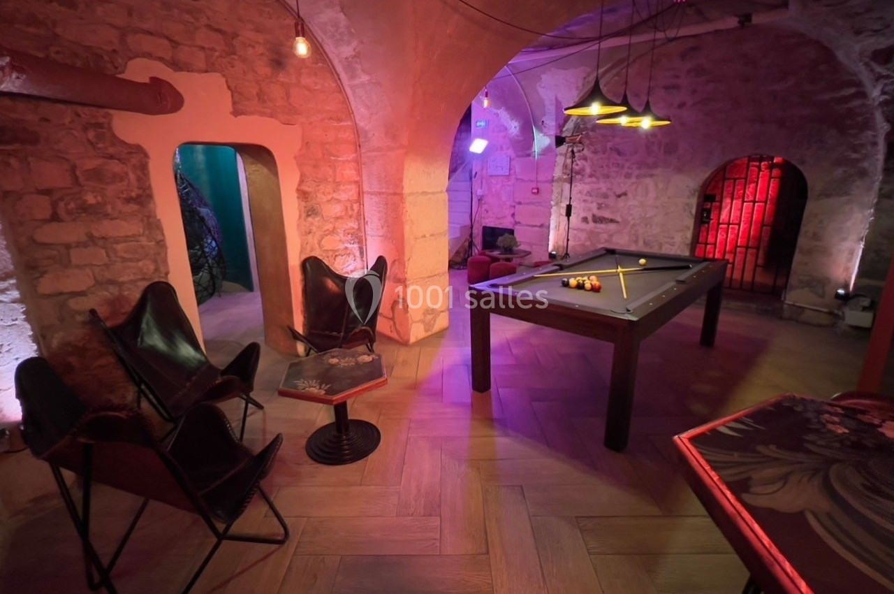 Salle voûtée en pierre avec table de billard, chaises en cuir, éclairage tamisé et ambiance chaleureuse.