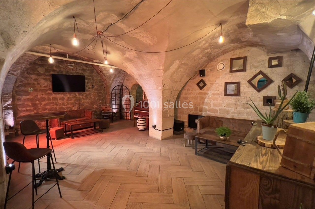 Salle voûtée en pierres apparentes avec mobilier en bois, éclairage tamisé et décorations murales.