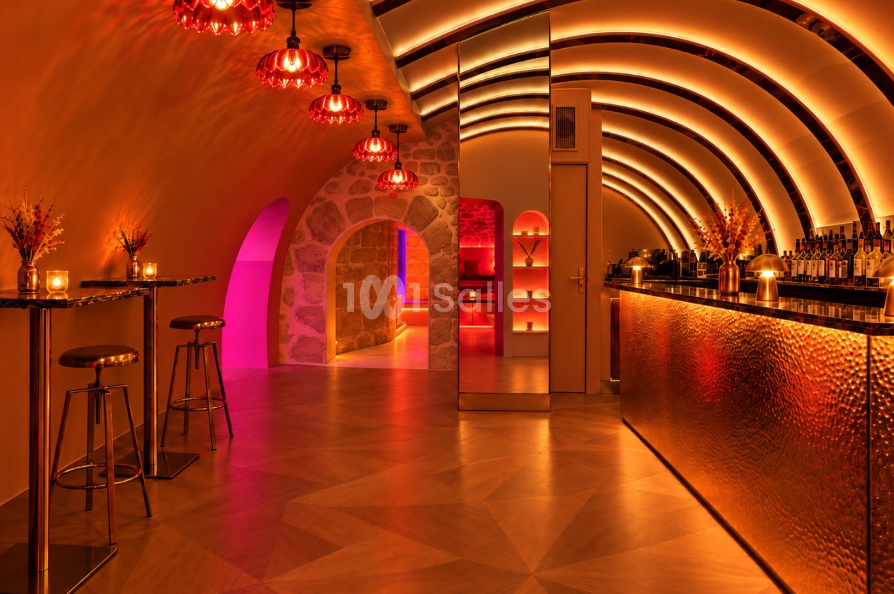 Bar en sous-sol aux voûtes arrondies éclairées en orangé, avec suspensions rouges, hauts tabourets et comptoir métallique martelé.