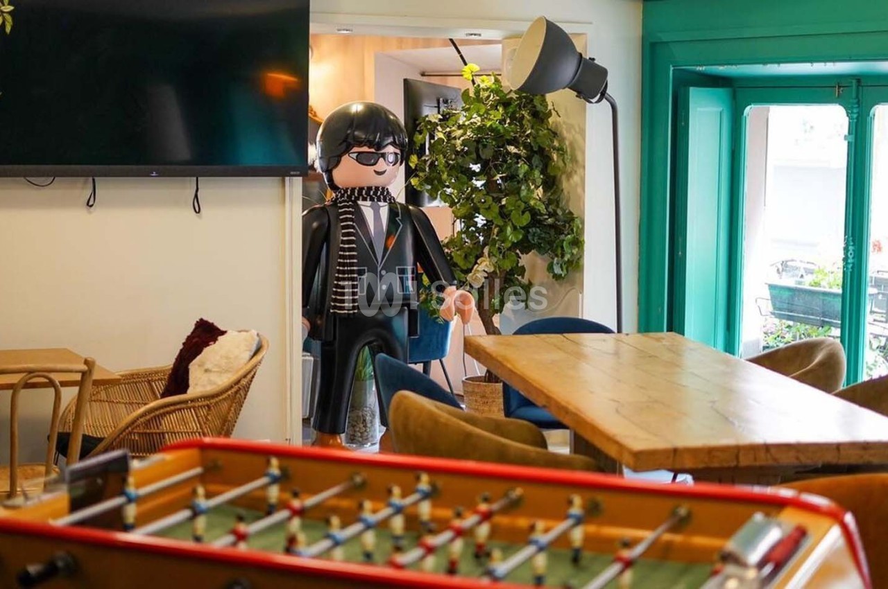 Un espace intérieur coloré avec des tables en bois, un baby-foot au premier plan et une grande figurine décorative.
