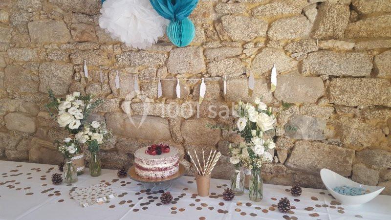 Décoration de table festive avec fleurs blanches, gâteau aux fruits rouges et guirlande sur un mur en pierre.