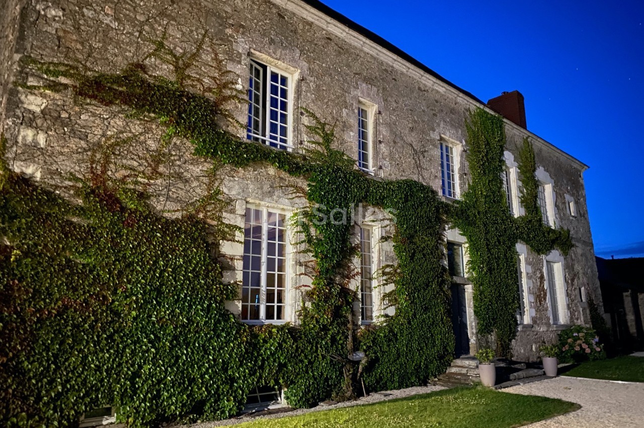Façade en pierre d'une maison ancienne recouverte de vigne vierge, éclairée à la tombée de la nuit.