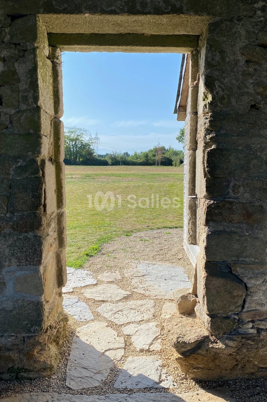 Vue à travers une porte en pierre ancienne donnant sur une pelouse ensoleillée et des arbres à l'arrière-plan.