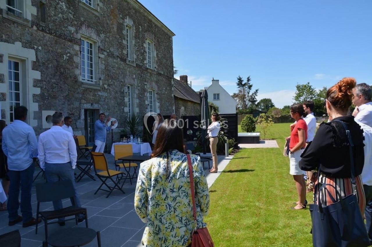 Un groupe de personnes debout et assises dans un jardin près d'un bâtiment en pierre par une journée ensoleillée.