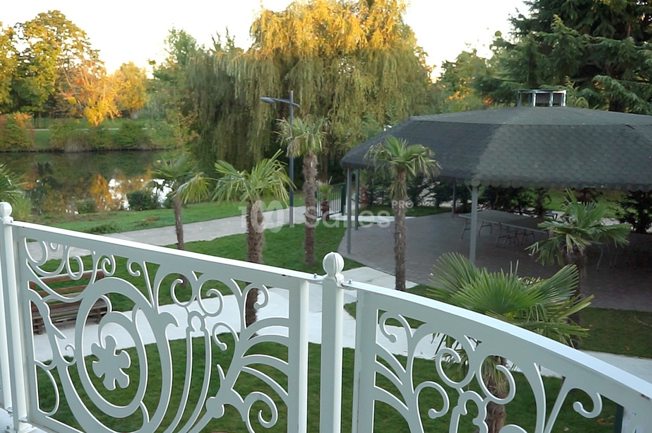 Vue depuis un balcon orné d'une balustrade blanche, donnant sur un jardin avec des palmiers, un étang et un kiosque.