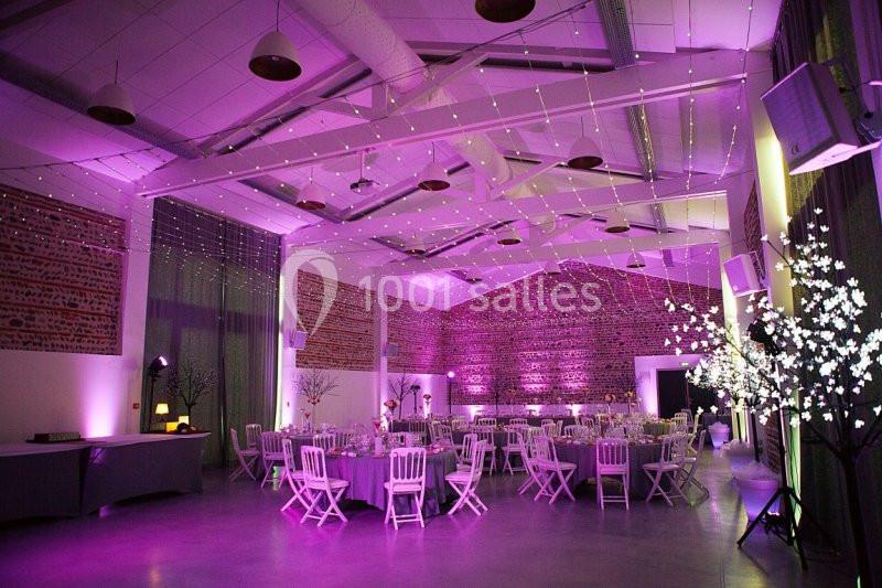 Salle de réception décorée avec des guirlandes lumineuses, des tables rondes et une ambiance lumineuse violette.