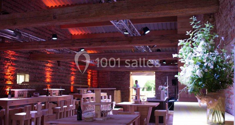 Salle en briques avec poutres apparentes, tables en bois, éclairage chaleureux et bouquet de fleurs blanches au premier plan.