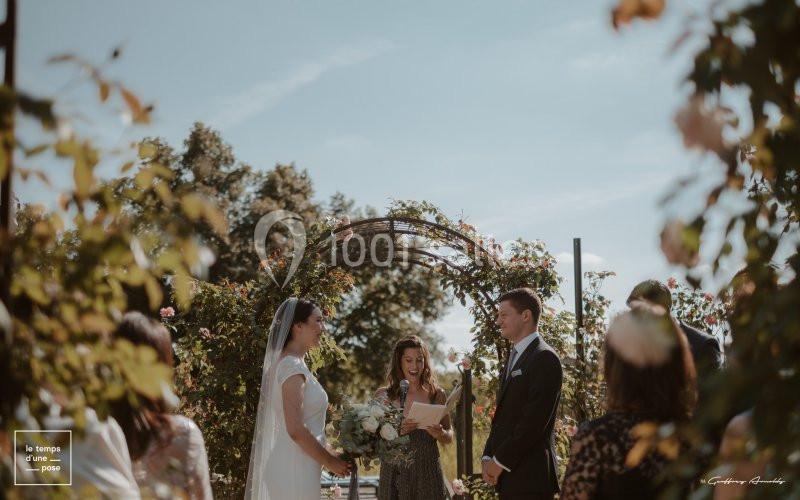 Un couple échange ses vœux sous une arche fleurie lors d'une cérémonie de mariage en plein air.
