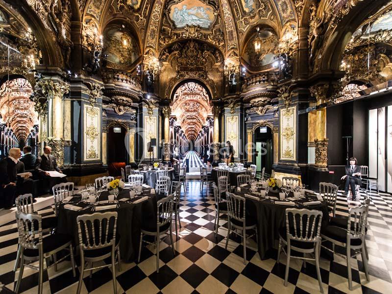 Salle de réception luxueuse avec plafond orné, tables dressées et sol en damier noir et blanc.