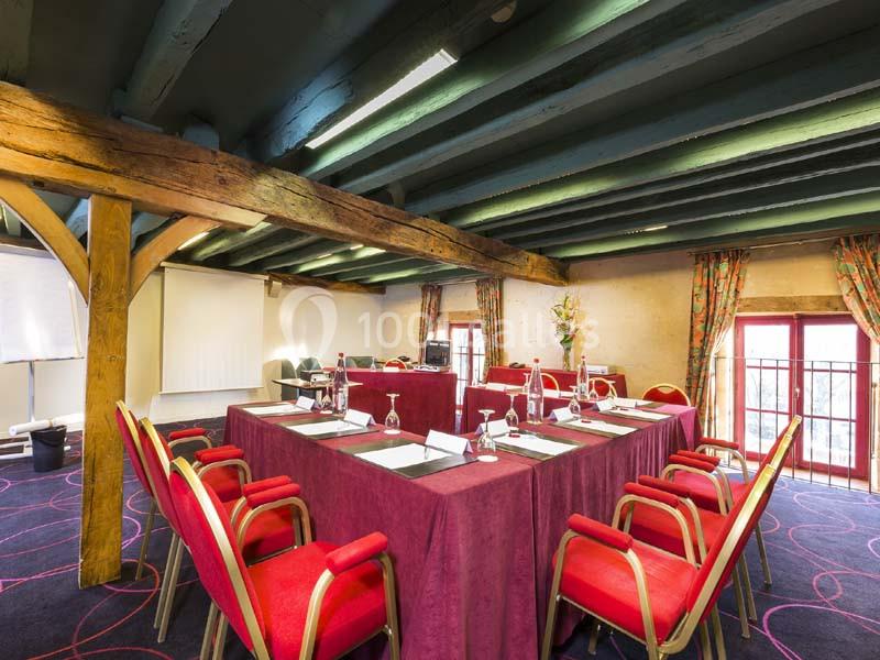 Salle de réunion avec poutres apparentes, tables disposées en U, chaises rouges et lumière naturelle provenant des fenêtres.