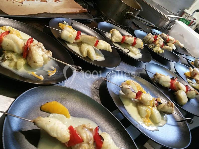 Location salle Bordeaux (Gironde) - Restaurant Le Family #24 Brochettes de poisson et légumes servies sur des assiettes noires avec une sauce et des morceaux d'orange.