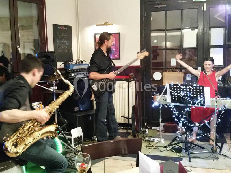 Location salle Bordeaux (Gironde) - Restaurant Le Family #28 Un groupe de musiciens joue en intérieur, avec un saxophoniste, un bassiste et une claviériste chantant.
