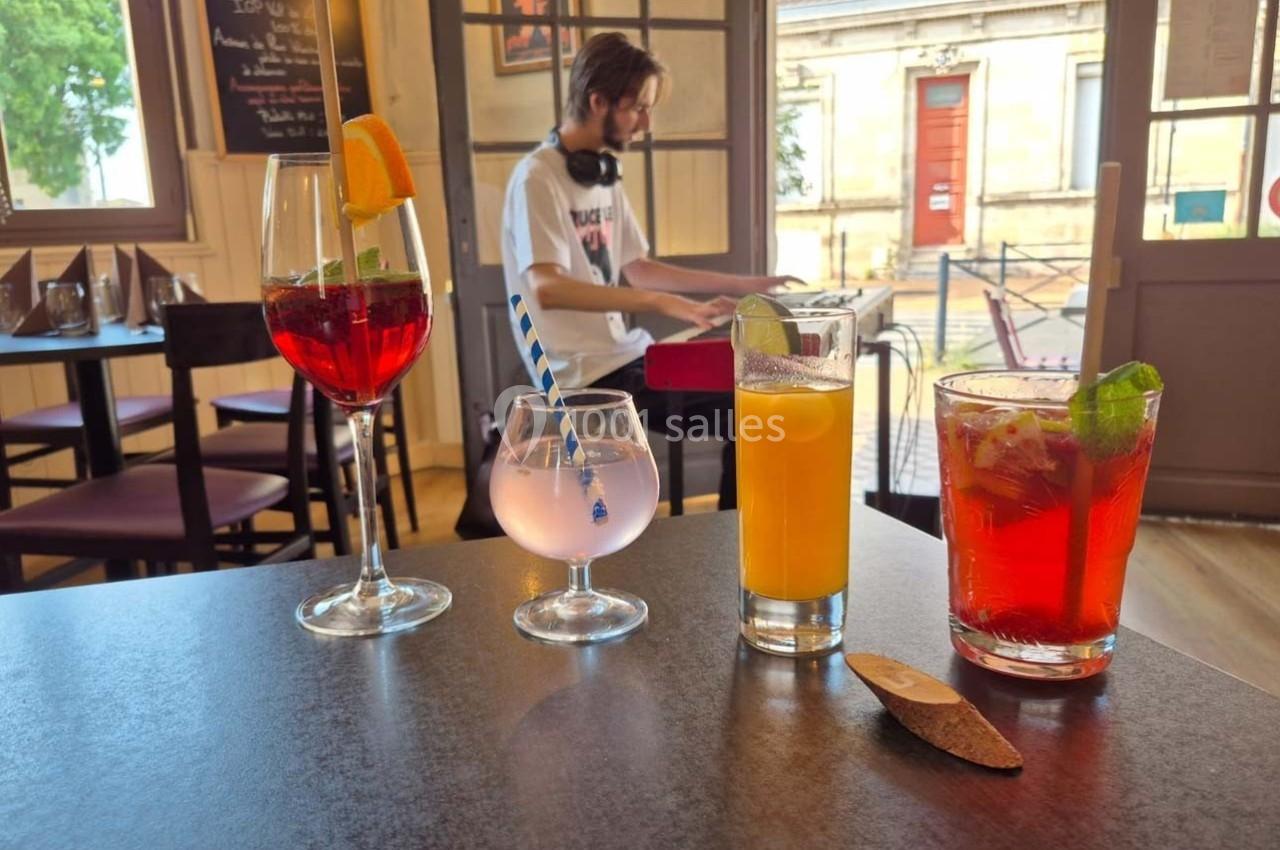 Location salle Bordeaux (Gironde) - Restaurant Le Family #10 Quatre boissons colorées sur une table dans un café, avec un musicien jouant du clavier en arrière-plan.