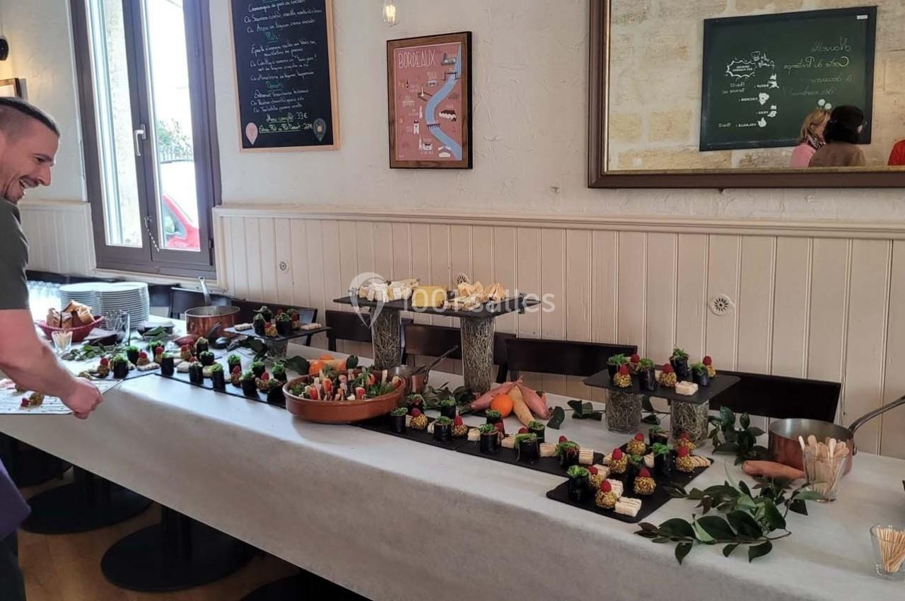 Location salle Bordeaux (Gironde) - Restaurant Le Family #13 Table garnie de plats variés et colorés dans un restaurant, avec un homme souriant ajustant la présentation.