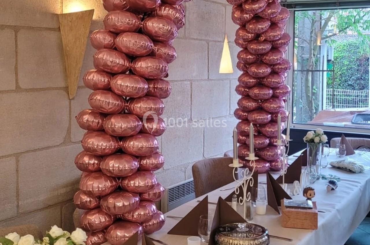 Location salle Bordeaux (Gironde) - Restaurant Le Family #2 Deux colonnes de ballons roses décorent une table de réception avec nappes blanches, bougies et pliages de serviettes.