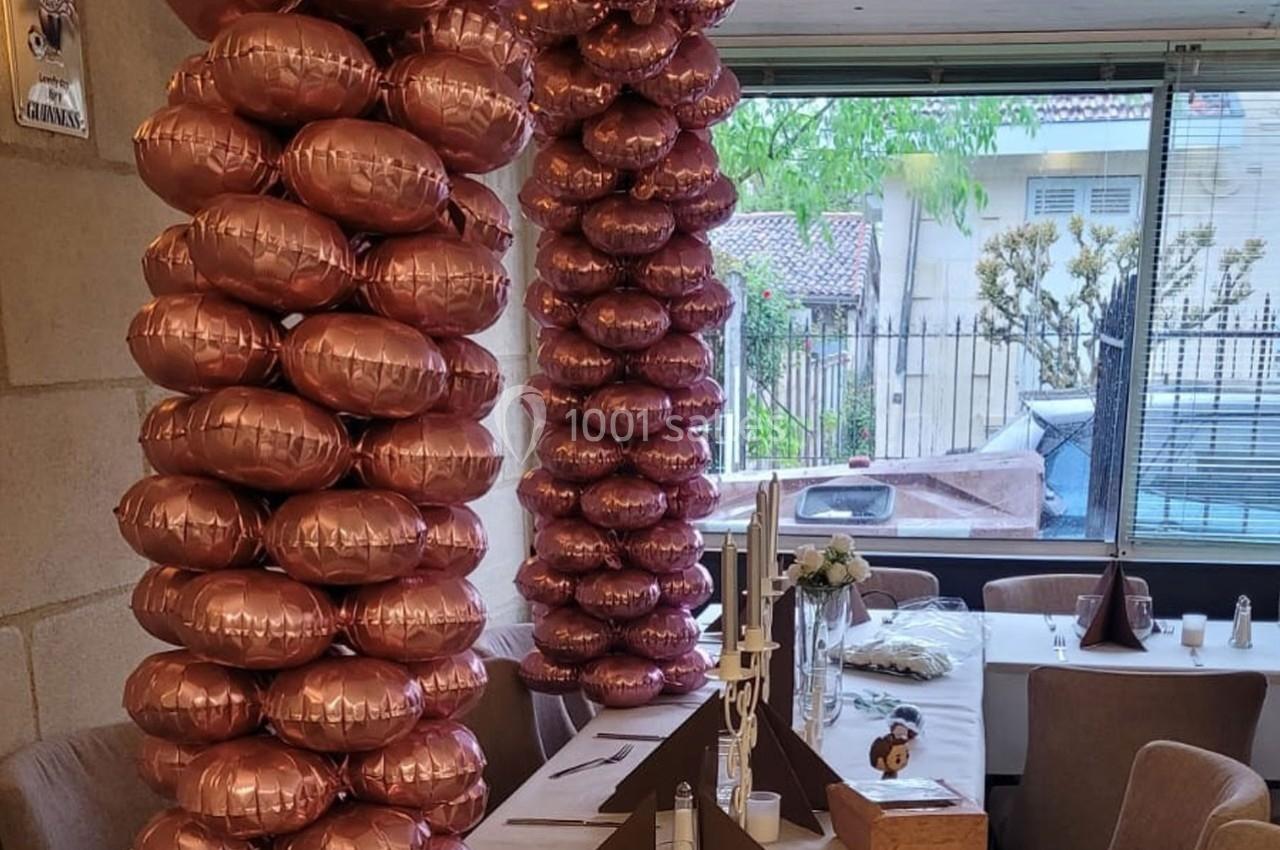Location salle Bordeaux (Gironde) - Restaurant Le Family #4 Deux colonnes de ballons roses métallisés décorent une salle avec des tables dressées près d'une baie vitrée.