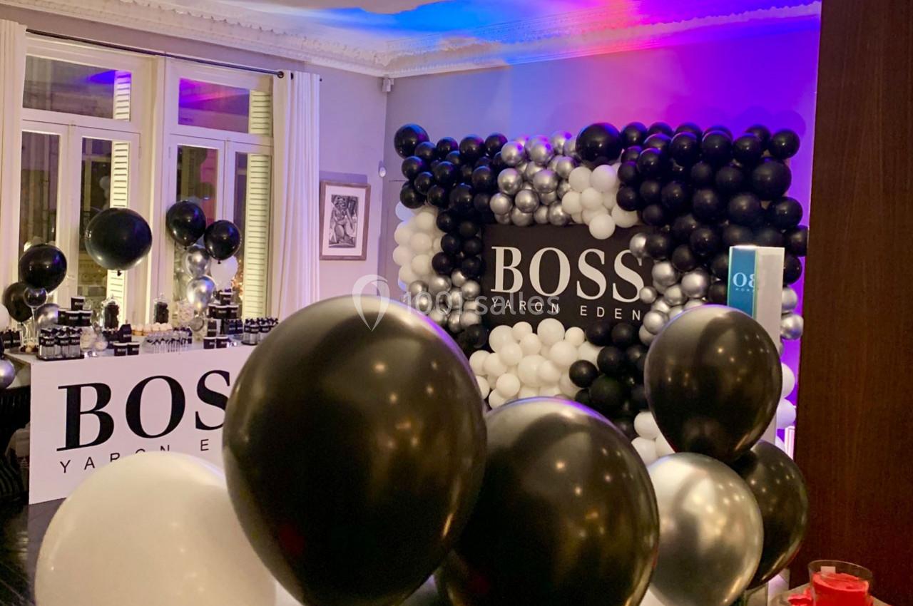 Décoration avec des ballons noirs, blancs et argentés autour d'un panneau ’Boss Yaron Eden’ dans une salle éclairée.