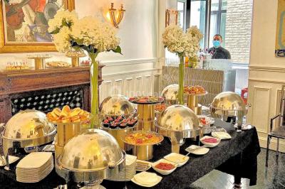 Table ronde en métal noir avec chandelier et chaises, placée sur un balcon avec vue sur une façade d'immeuble haussmannien.