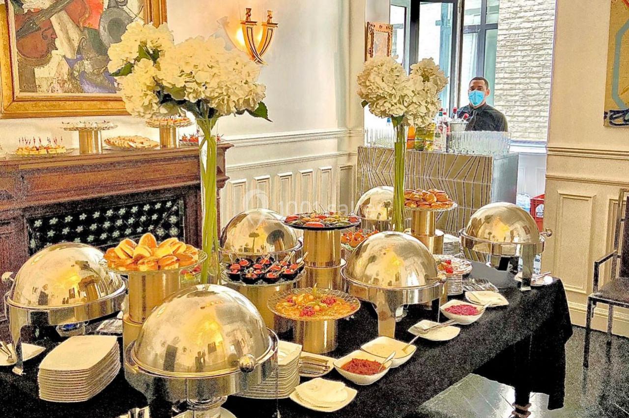 Buffet élégant avec plats variés sous cloches, fleurs blanches en décoration et un serveur en arrière-plan.
