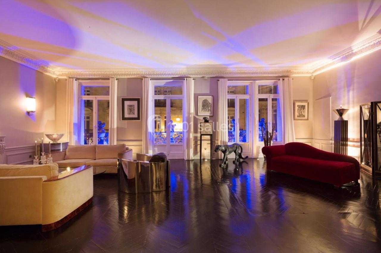 Salon spacieux avec parquet sombre, canapés élégants, sculptures modernes et éclairage tamisé aux tons violets.