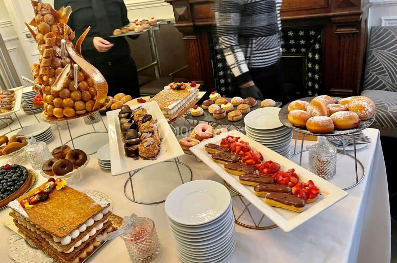 Table garnie de pâtisseries variées, dont éclairs, mille-feuilles, donuts et pièce montée, dans un cadre élégant.