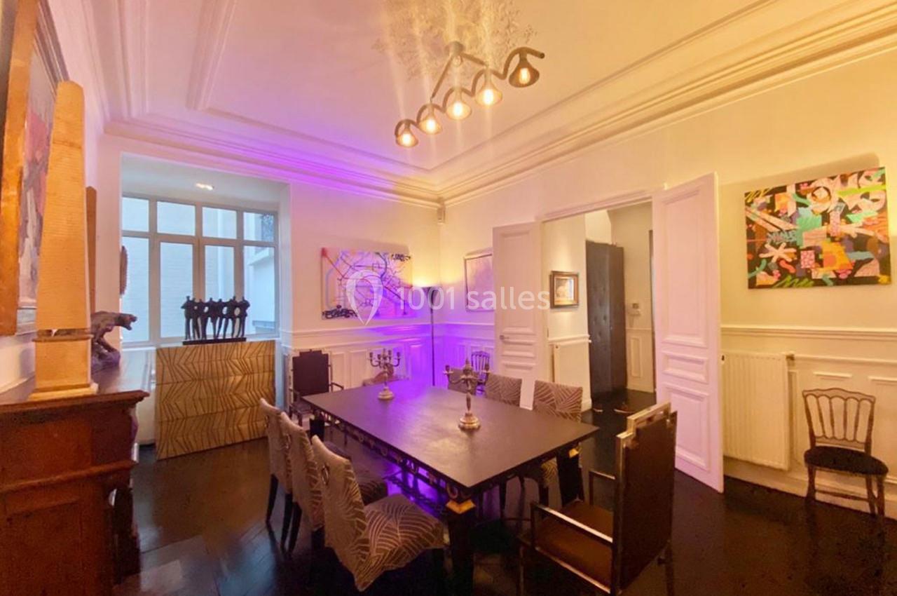 Salle à manger avec table rectangulaire, chaises variées, éclairage chaleureux et œuvres d'art aux murs.