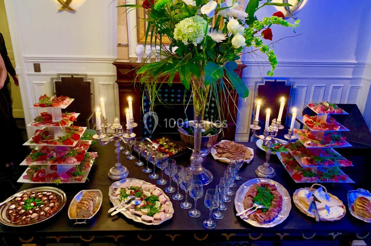 Table garnie de plats variés, bougies allumées et grand bouquet floral au centre dans une salle élégante.